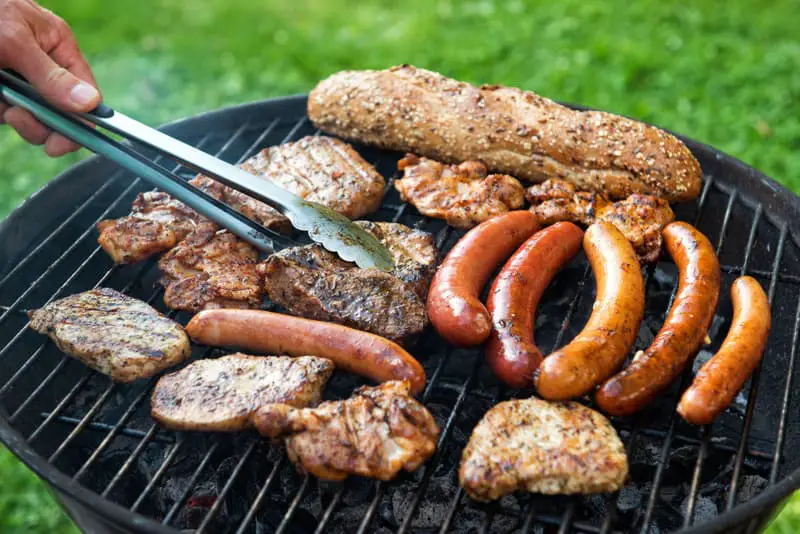 Canva Assorted meat and sausage on grill with the coals cooking outdoors