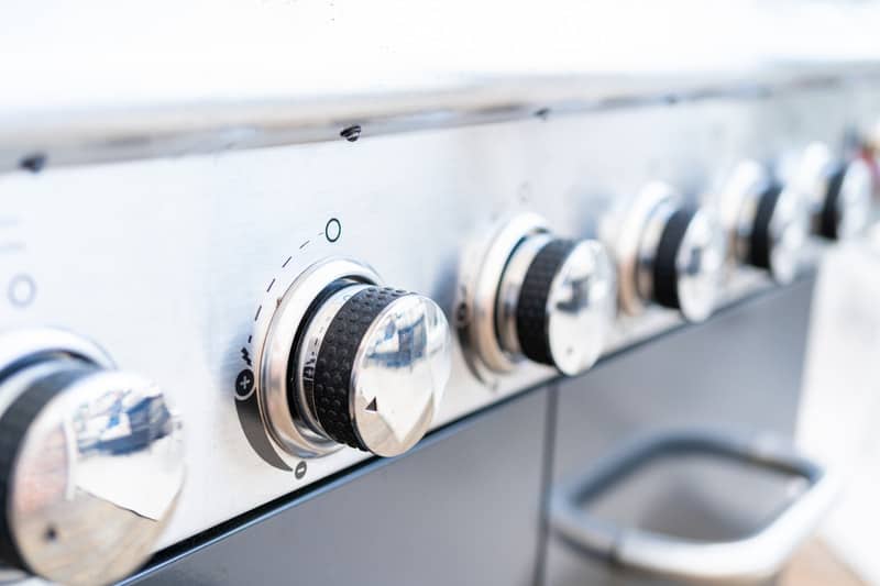 Canva Close up of control knobs on an outdoor gas grill.