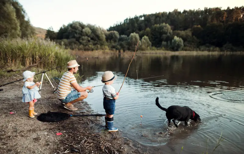 Canva A Mature Father with Small Toddler Children and a Dog Fishing by a Lake.