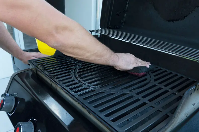 Canva A man washes a black street grill with a soft sponge. Grill preparation for frying meat.